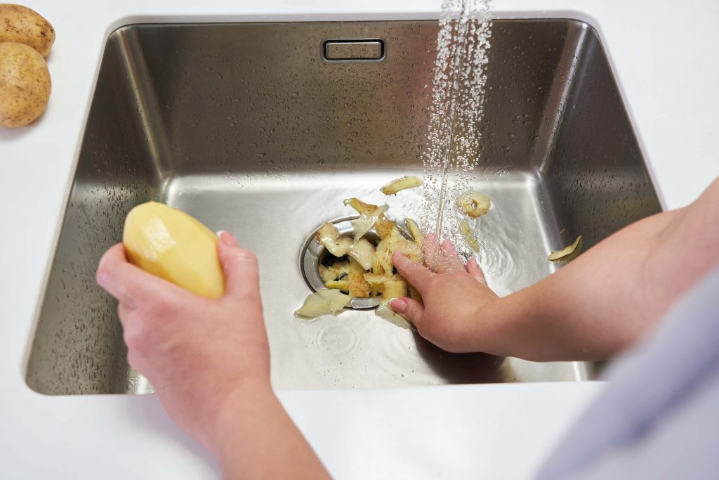 Person shoving potato peels down garbage disposal