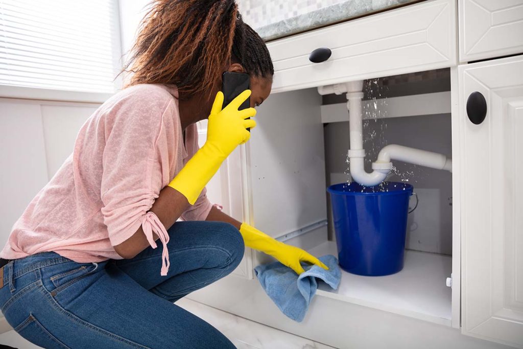 Young woman putting bucket under leaking sink pipe