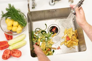 A person washing food scraps down the garbage disposal.